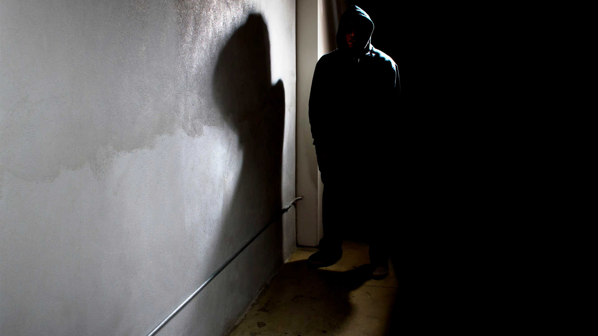 hooded criminal stalking in the shadows of a dark street alley